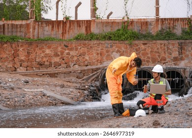 Two environmental field workers in protective gear conduct a water pollution inspection at a drainage outlet, collecting samples and analyzing data for contamination levels.