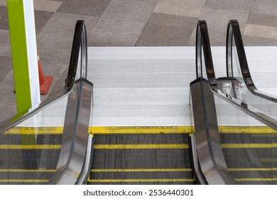 Two escalators are side by side, one of which is yellow and the other is black. The escalators are in a public area, possibly a mall or a train station