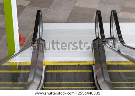 Two escalators are side by side, one of which is yellow and the other is black. The escalators are in a public area, possibly a mall or a train station