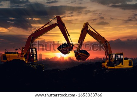 Two Excavators are digging the soil in the construction site on the sky sunset with cityscapes background