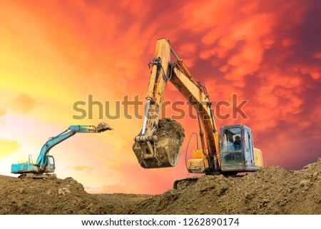 Two excavators work on construction site at sunset