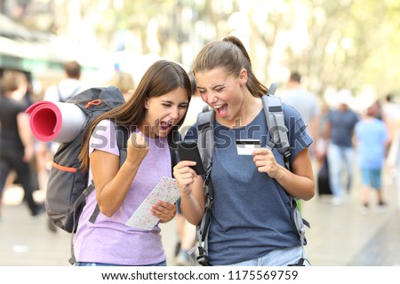 Two excited backpackers buying online with credit card and a smart phone in the street