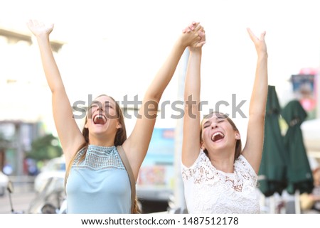 Two excited friends celebrating success raising arms together outdoors in the street