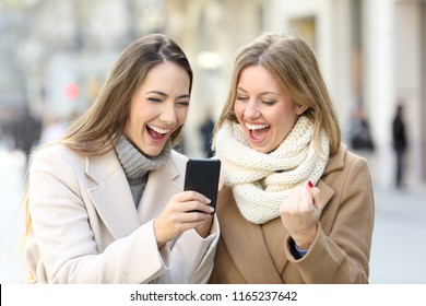 Two Excited Friends Reading Phone Content In Winter In The Street