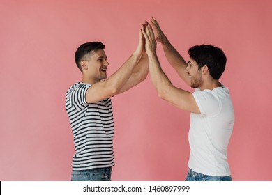 Two Excited Friends Touching Hands And Looking At Each Other Isolated On Pink