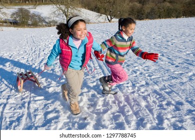Two excited girls on winter vacation pulling sled up snowy hill