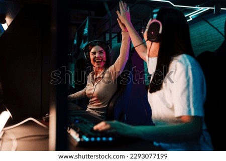 Two excited young girls giving high five to each other while playing online video game on championship in modern cybersport club
