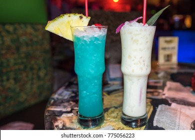 Two Exotic Tiki Drinks On A Table In A Dark Tiki Bar.