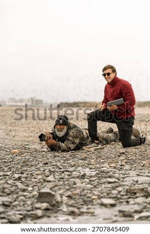 Two experienced bird enthusiasts observing and photographing birds in a natural marsh environment, sharing a love for nature