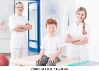 Two Experienced Physiotherapists And Little Red Head Boy In Pediatric Rehabilitation Clinic