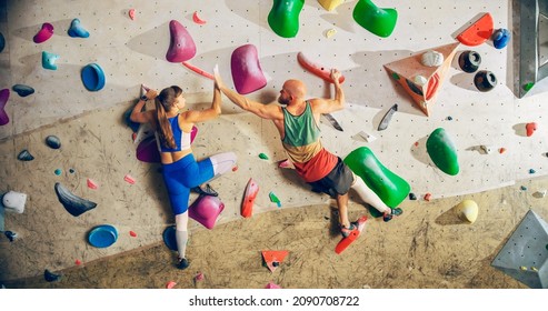 Two Experienced Rock Climbers Practicing Climbing on Bouldering Wall in a Gym. Friends Exercising at Indoor Fitness Facility, Doing Extreme Sport for Healthy Training. Giving Each Other High Five. - Powered by Shutterstock