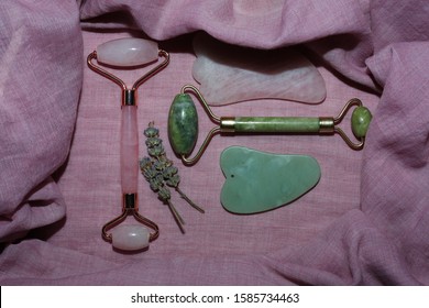 Two face rollers pink and green on pink cotton background. Face massagers flat lay.
