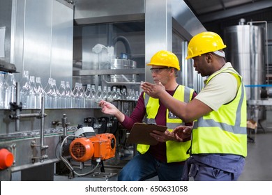 Two factory workers discussing while monitoring drinks production line at factory - Powered by Shutterstock