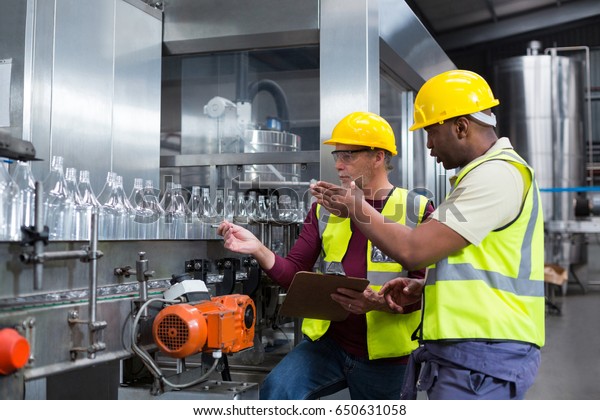 Two factory workers discussing while\
monitoring drinks production line at\
factory