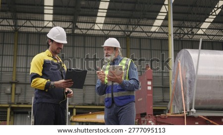 Two factory workers inspecting cargo data on a tablet in a warehouse, collaborating on logistics and supply chain management for industrial freight shipment.