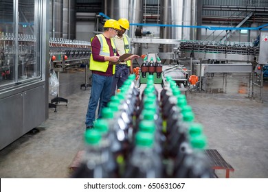 Two factory workers monitoring cold drink bottles on production line at drinks production plant