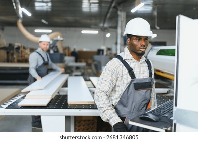 Two factory workers operating a cnc machine in a furniture factory, producing wooden parts for sofas and other furniture