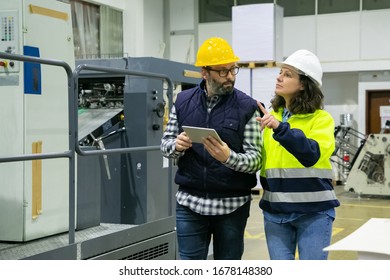 Two Factory Workers With Tablet Inspecting Equipment. Concentrated Woman Pointing At Printing Machine. Print Manufacturing, Technology Concept