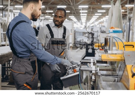 Two factory workers in uniform operating a machine in a modern industrial production plant for aluminum and pvc windows and doors