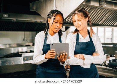 Two famous chefs discuss video blog in a professional stainless steel kitchen using a tablet. Professionals smiling searching reading communicating with modern technology. - Powered by Shutterstock