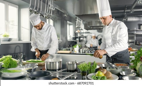 Zwei berühmte Köche arbeiten als Team in einem großen Restaurant Küche. Gemüse und Zutaten sind überall, Küche sieht modern aus mit viel Edelstahl.