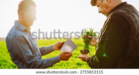 Two farm workers with a digital tablet and a green plant work in a field at sunset. Agronomists check crop growth and conduct farming. Concept of agriculture and gardening.