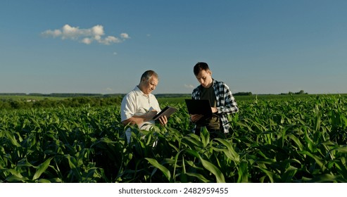 Two farmers from different generations collaborating in a cornfield, using a laptop. Concept of learning and knowledge transfer - Powered by Shutterstock - Get 15% off with code: PIKWIZARD15