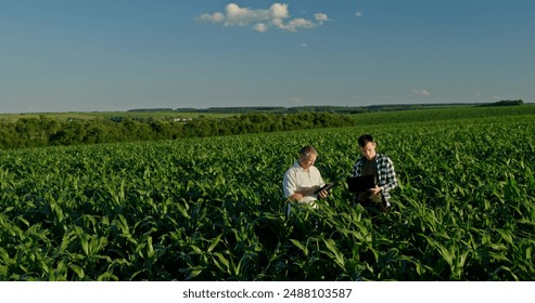 Two farmers from different generations collaborating in a cornfield, using a laptop. Concept of learning and knowledge transfer - Powered by Shutterstock