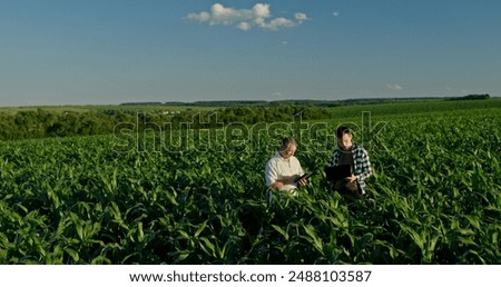 Two farmers from different generations collaborating in a cornfield, using a laptop. Concept of learning and knowledge transfer