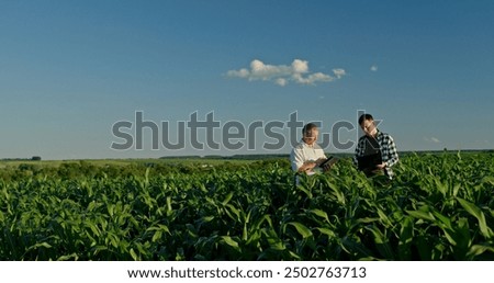 Two farmers from different generations collaborating in a cornfield, using a laptop. Concept of learning and knowledge transfer