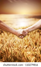 Two farmer's hands handshake at the harvest of wheat field.