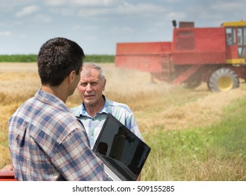 Two Farmers Talking In Wheat Field In Front Of Combine Harvester