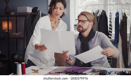 Two fashion designers comparing sketches on paper working in sewing atelier, clothes creating concept - Powered by Shutterstock