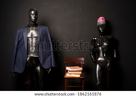 Two fashion dolls each with a single clothing item standing next to a chair with several books