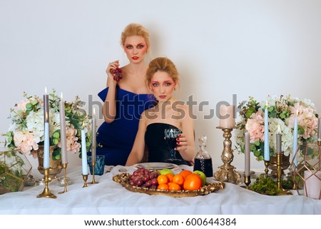 Two fashion models behind the table with fruits, candles and wine.