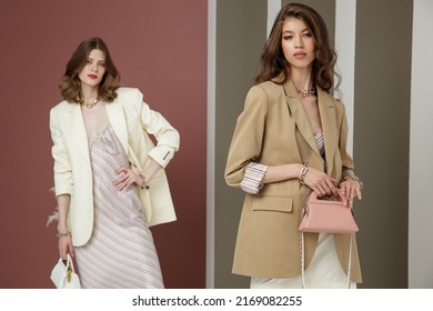 Two Fashion Models In White Cream And Sand Brown Looks. Jacket, Blazer, Skirt, Long Dress, Handbag. Beautiful Young Women. Rosy Brown And Striped Corrugated Wall, Dry Branches. Asian, European Girls