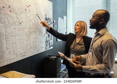 Two FBI agents looking at map on board while mature female pointing at it and making suggestions about possible location of criminal