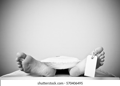 Two feet of a dead body, with an identification tag - blank sign attached to a toe. Covered with a white sheet.
