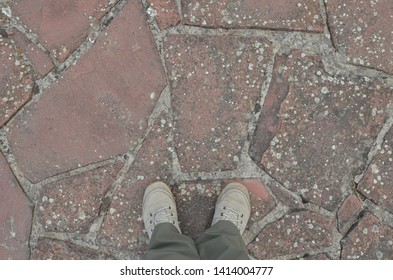 Two Feet In White Canvas Shoes Standing On Grit Stone Sidewalk. Directly Above View. 