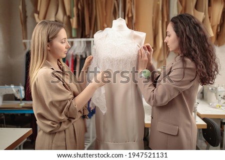 two femail Dressmakers or tailors or fashiondesigners or seamstresses picking a tailor dummy mannequin in a lace cloth at own workshop studio. Small handmade business concept
