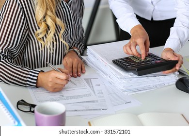 Two female accountants counting on calculator income for tax form completion hands closeup. Internal Revenue Service inspector checking financial document. Planning budget, audit concept
