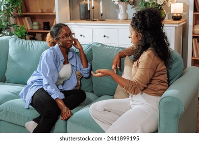 Two female African american best friends talking about a serious topic while sitting on the sofa in the living room - Powered by Shutterstock