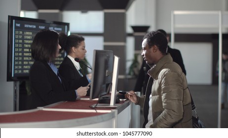 Two Female Airport Security Personnel Checking Identification At A Check-in Or Boarding Counter At The Departure Terminal Holding The Passports Of Two Male Passengers