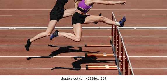 two female athletes running hurdles in athletics competition, hurdling on stadium track, summer sports games - Powered by Shutterstock