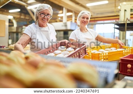 Two female bakers carry freshly baked Berlin pancakes in boxes in a large bakery