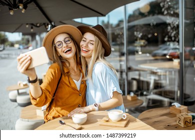 Two female best friends making selfie portrait while spending time together on the cafe terrace during a summer day - Powered by Shutterstock