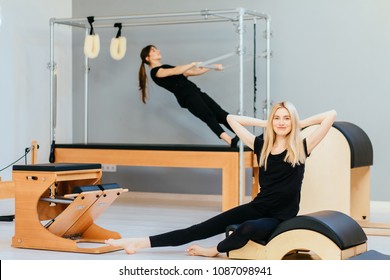 Two Female In Black Sportswear Working Out On Spine Corrector And Cadillac - Modern Pilates Equipment In Gym. Health And Rehabilitation Concept.