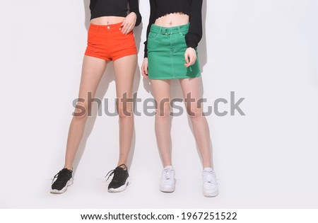 Two female in black sweater with fashion  blue skirt and orange shorts with black and white shoes, posing in studio