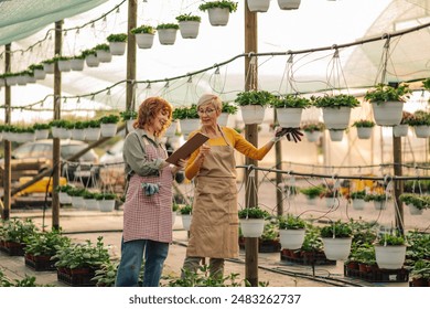 Two female botanists are examining plants in there vertical garden greenhouse. Senior botanist helping young gardener take notes on sapling progress on clipboard. Botanists discussing plant growth. - Powered by Shutterstock