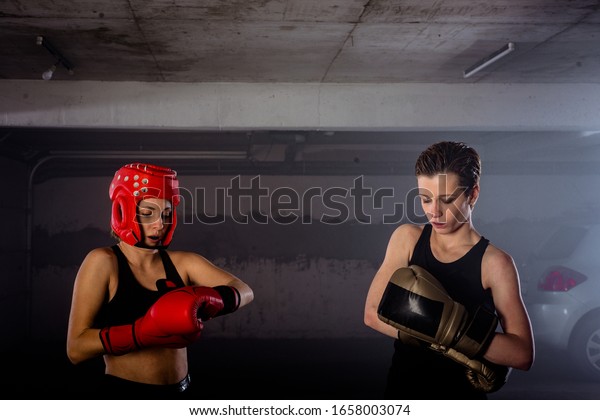 Two female boxers putting on boxing gloves before\
their fight inside a garage